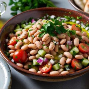 Ein erfrischender weißer Bohnensalat inspiriert von Ful Medames, mit Kirschtomaten, Gurken und Kräutern. Dazu passt frisches Pita-Brot und ein kleines Glas Olivenöl.